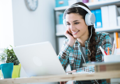 Teenage smiling girl using a laptop and wearing headphones, technology and leisure concept