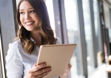 Young businesswoman using a digital tablet while standing in front of windows in office