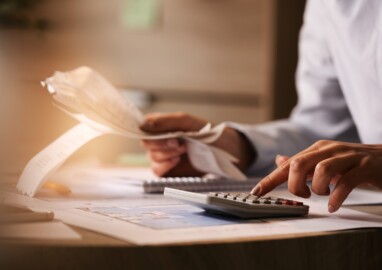 Close-up of economist using calculator while going through bills and taxes in the office.
