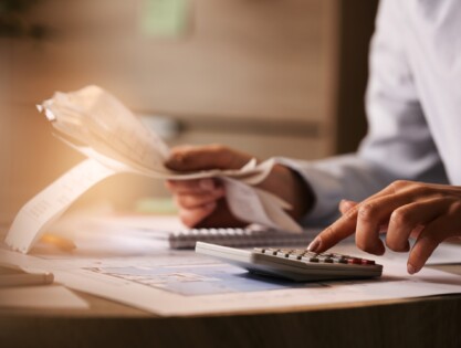Close-up of economist using calculator while going through bills and taxes in the office.