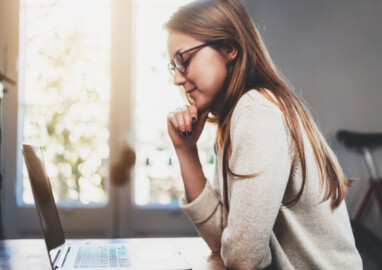 Side view shot of smiling hipster girl talking with friends via an app on laptop, cheerful female student with long hair studying via portable computer at coffee shop, woman freelancer working from home on notebook